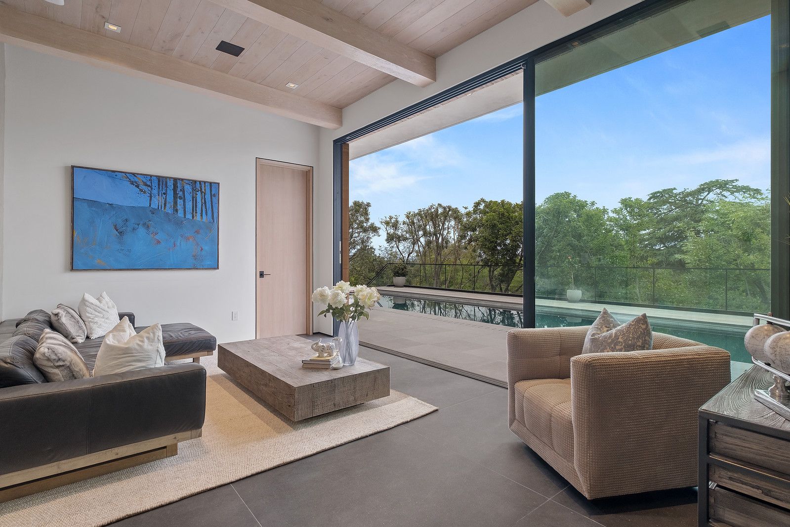 Living room with a wood beam ceiling and a floor-to-ceiling sliding glass wall open to trees