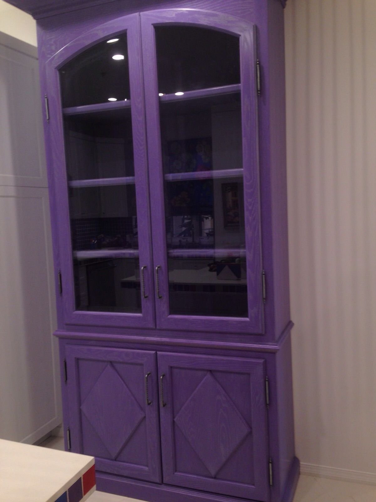 Tall purple painted cabinet with arched glass doors above and diamond-panel doors below