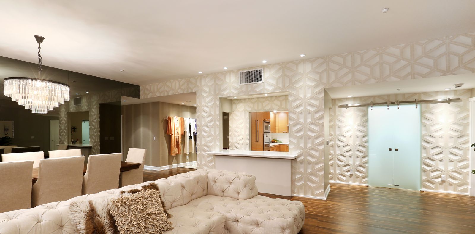 Condo living and dining room with a crystal chandelier, white geometric wall panels, a kitchen pass-through and frosted glass sliding doors